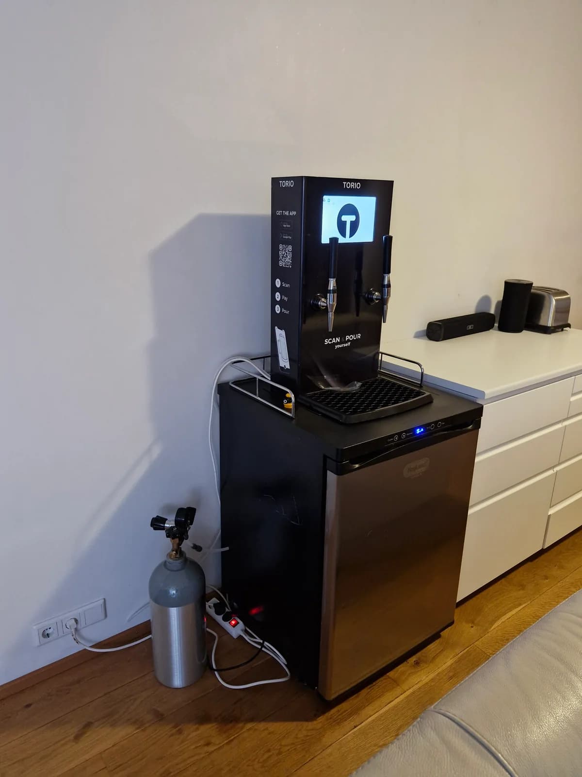 The assembled dispenser above a fridge, with its screen on and plumbing connected.